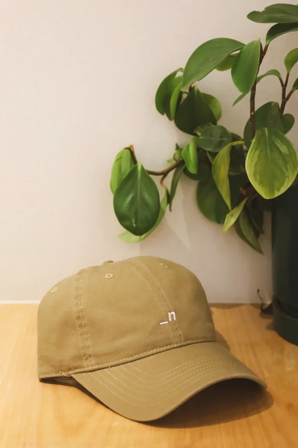 Olive Noia cap with _n logo beside a trailing plant